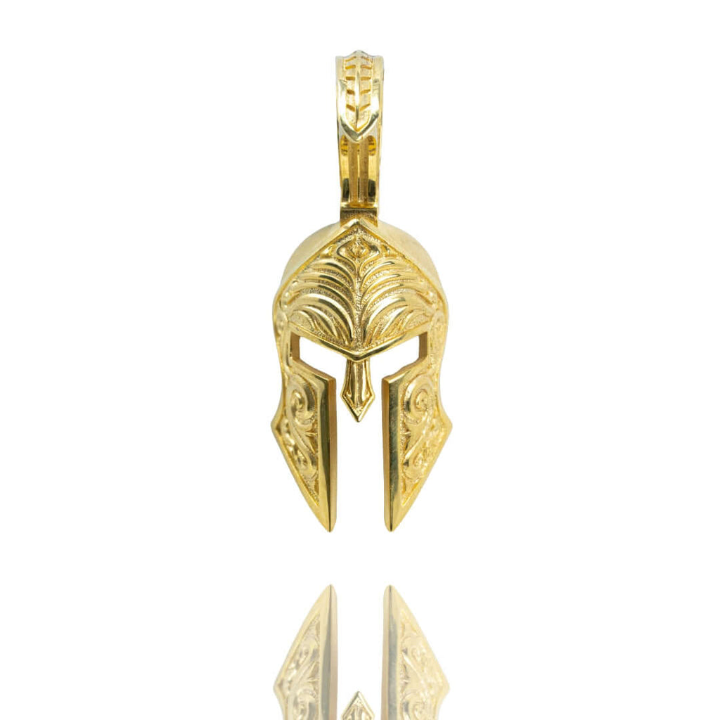 The Spartan Helmet Pendant - 14k Solid Gold features an ancient warrior helmet design with intricate engravings, shown against a white background with a subtle reflection.