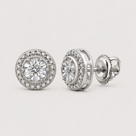 A pair of 0.01CTW Diamond Round Earrings in sterling silver is shown on a reflective circular surface against a warm off-white studio background.