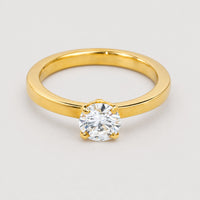 A 0.73ct round lab diamond solitaire engagement ring in 14k gold, set with a single brilliant-cut diamond in four prongs and showcased against a plain, light gray background.