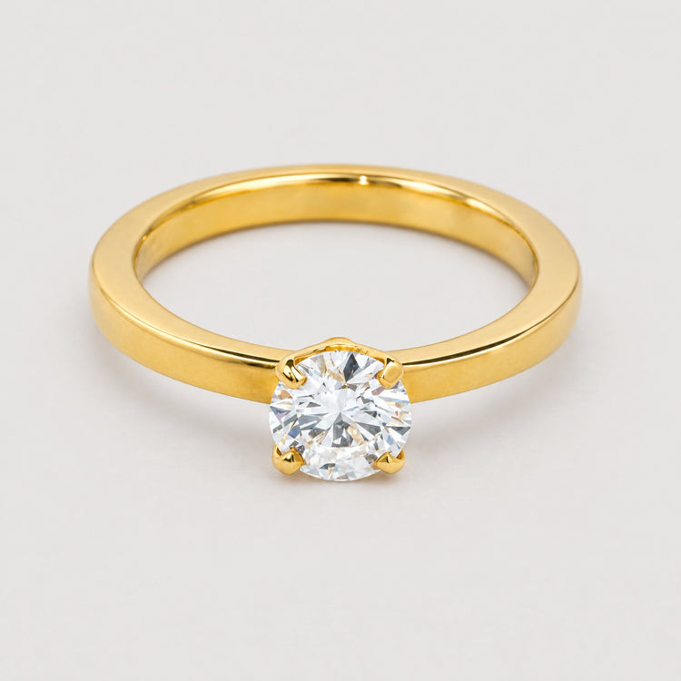 A 0.73ct round lab diamond solitaire engagement ring in 14k gold, set with a single brilliant-cut diamond in four prongs and showcased against a plain, light gray background.