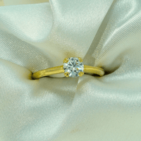 A 0.73ct Round Lab Diamond Solitaire Engagement Ring in 14k gold rests on pale, shimmery satin. Centered in the image, this elegant piece for women sparkles as the diamond catches the light.