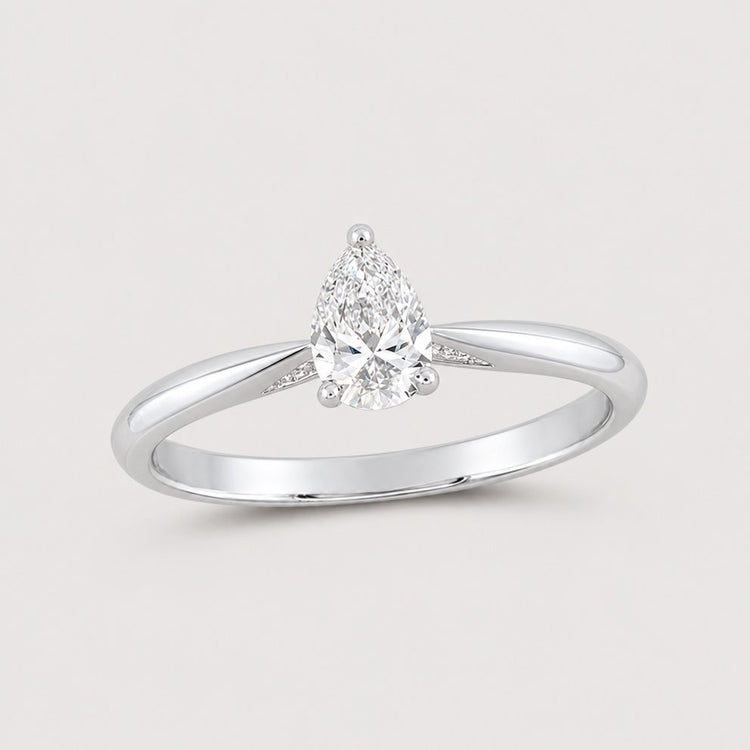 The 1/2CT Pear Diamond Solitaire Ring in 14k Gold, showcasing a single natural diamond on a slender gold band, is elegantly displayed against a warm off-white studio background.