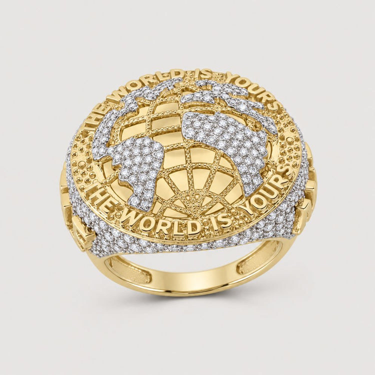 The 1 3/8CTW Diamond Men’s Ring in 10k yellow gold features a raised globe motif, natural diamond accents, and “THE WORLD IS YOURS” engraved around the top edge.