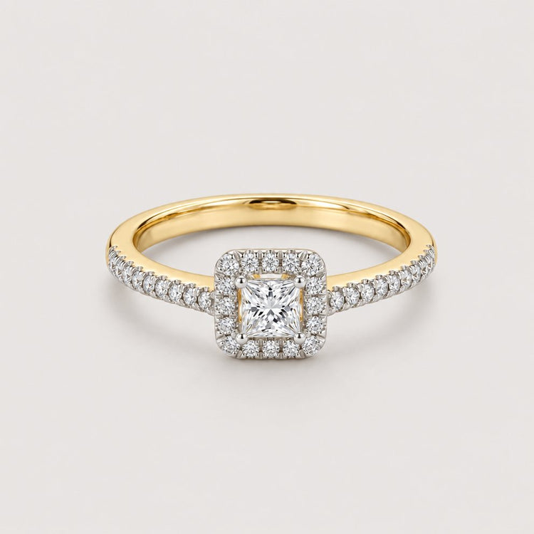 The 10k Gold Princess Diamond Halo Engagement Ring features a square-cut center diamond, a halo of 1/3 Cttw diamonds, and additional diamonds set along the upper half of the band.