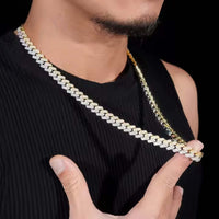 A person in a sleeveless black shirt showcases the Moissanite Cuban Link Chain - 10mm, holding the sparkling gold and silver necklace against a black background.