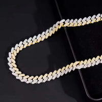 The Moissanite Cuban Link Chain - 10mm features sparkling VVS moissanite stones set in 925 sterling silver and gold, shown close-up on a dark reflective surface.