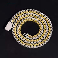 The Moissanite Cuban Link Chain - 10mm features interlocking gold and 925 sterling silver links, coiled in a spiral on a black background with the clasp visible at one end.