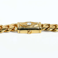 The Cuban Link Chain Evil Eye Lock 14k Gold - 12mm features thick, polished links and a rectangular clasp with an Evil Eye lock, adorned with a clear central gemstone for a striking, shiny finish.