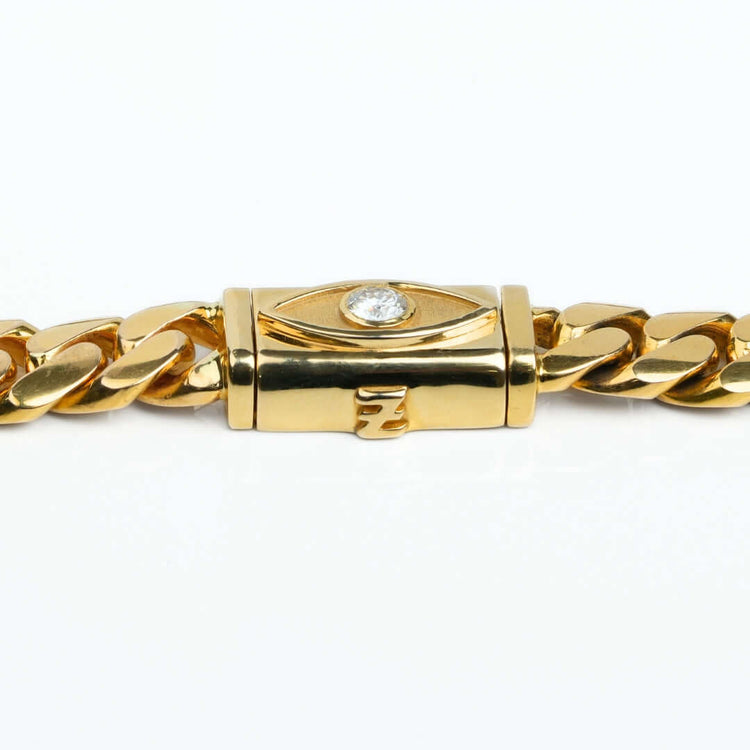 The 12mm Handmade Miami Cuban Link Chain with Evil Eye Lock is crafted in 14K solid gold and features a rectangular clasp adorned with a diamond set in an eye-shaped Evil Eye design, plus an engraved detail beneath the diamond.