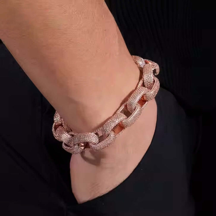 A person wears the Silver Moissanite Bracelet Rose Gold -13mm, featuring chunky links encrusted with sparkling stones, with their hand tucked into the pocket of black pants.