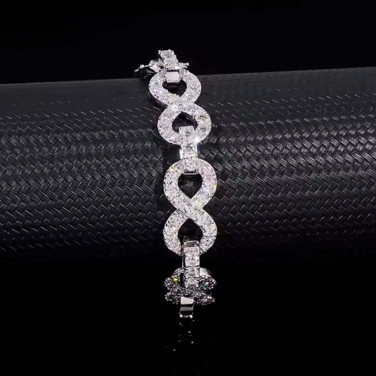 The Silver Moissanite Infinity Bracelet - 13mm features sparkling, interlocking infinity links encrusted with clear gemstones, beautifully displayed on a textured black surface.