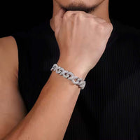 A person in a sleeveless black top raises their hand near their face, showcasing the Silver Moissanite Infinity Link Chain -13MM on their left forearm against a deep black background.