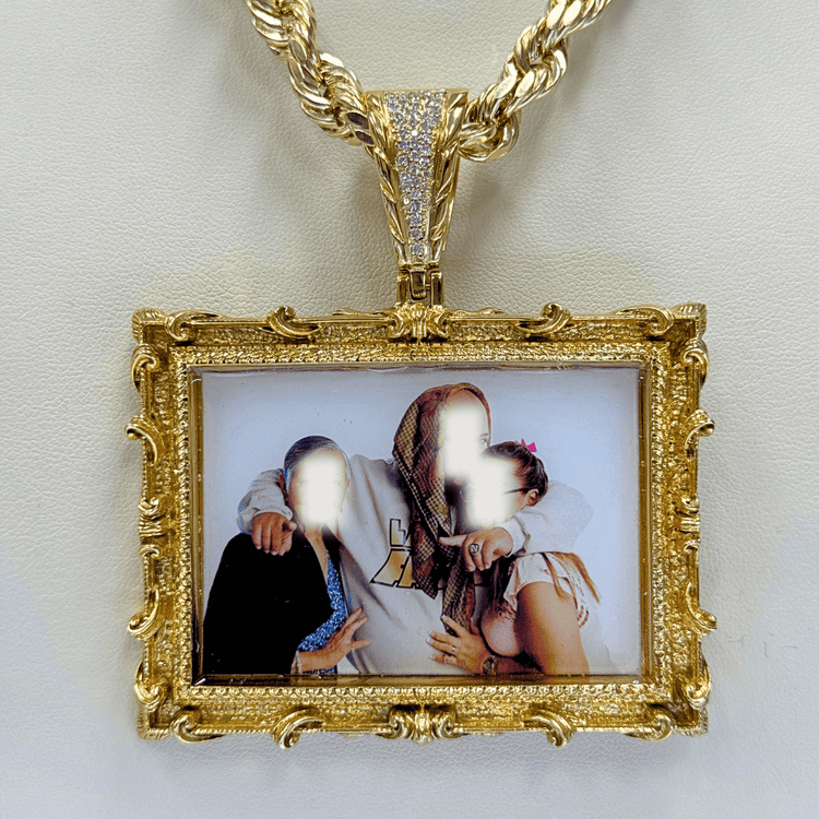 The 14K Gold Diamond Bail Big Frame Picture Pendant hangs on a thick chain, displaying a blurred photo of three people—one in a brown patterned hood—resting on a white background.
