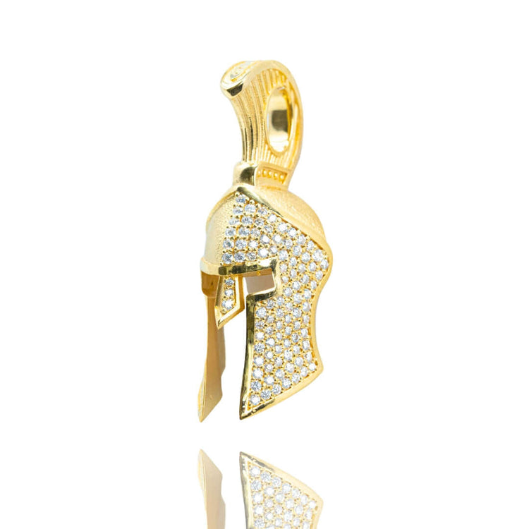 The Half-Face Diamond Spartan Helmet Pendant in 14K Gold features a helmet design adorned with sparkling white stones, displayed against a white background with a subtle reflection beneath.