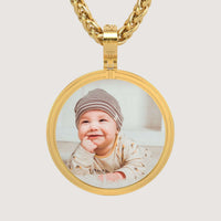 The 14K Gold Modern Double Border Round Picture Pendant features a smiling baby in a striped hat and light clothes, lying down and looking upward—making it a charming way to cherish special moments.
