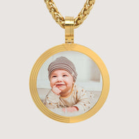 The 14K Gold Modern Grooved Round Picture Pendant displays a cherished baby photo in a stylish setting, elegantly hung on a matching chain.