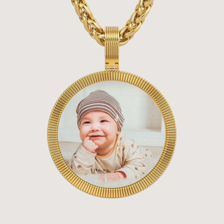 The 14K Gold Ribbed Round Picture Pendant features a customizable charm, shown here with a photo of a smiling baby in a striped hat and light-colored outfit, resting on their stomach.