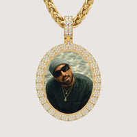 The 14K Gold Scalloped Oval Diamond Photo Pendant features a diamond-encrusted oval frame and showcases a photo of a man in a beanie, sunglasses, and layered necklaces gazing up at the camera.