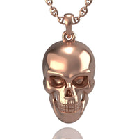 The 14k Gold Skull Pendant features a shiny, metallic human skull design and hangs from a matching chain necklace, displayed against a white background.