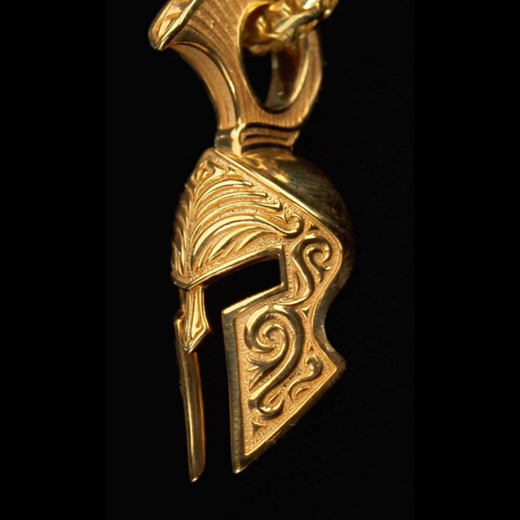 A close-up of an ornate ancient Greek-style helmet with a raised crest, set against black—reminiscent of the Spartan Helmet Pendant in 14k solid gold.