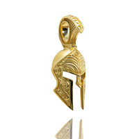 The Spartan Helmet Pendant - 14k Solid Gold is shaped like an ancient Greek warrior’s helmet, features detailed engraved patterns, and includes a loop for a chain. It’s photographed against a white background.