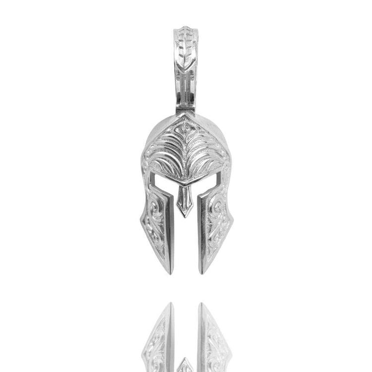 The Spartan Helmet Pendant - 14k Solid Gold features intricate detailing in the shape of an ancient Greek or Spartan helmet, photographed on a white background with its reflection—a bold piece of jewelry for any warrior at heart.
