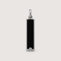 A rectangular black enamel pendant framed in 14k gold, adorned with a small round white gem at the base, hangs from a gold loop against a plain light background. This elegant piece embodies the timeless allure of the 14k Gold Black Enamel Tag Pendant with its sleek and sophisticated design.