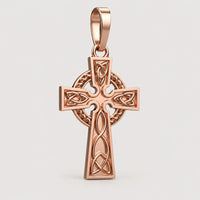 The 14k Gold Celtic Cross Pendant features detailed knotwork and a chain loop, showcased elegantly on a warm off-white studio background.