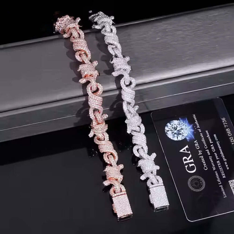 The Twisted Infinity Thorn Moissanite Bracelet (15mm) sparkles with moissanite stones and is shown beside a black GRA diamond certification card on a reflective surface.