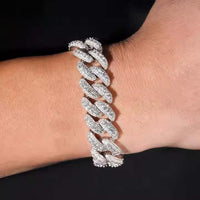 A close-up of a wrist wearing the Silver Moissanite Cuban Link Bracelet - 16mm, encrusted with sparkling stones, displayed against a black background.