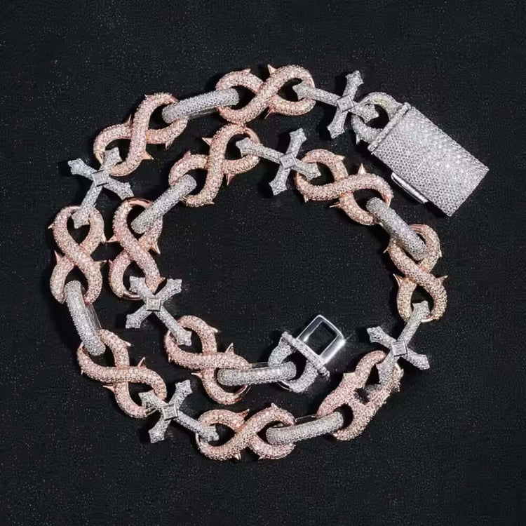 The Two-Tone Cross Moissanite Necklace-16mm, featuring alternating interlocking and cross-shaped links with sparkling stones, is displayed on a black textured surface.