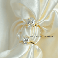 Two 1.72ct oval-cut lab diamond engagement rings in 14k solid yellow gold rest elegantly on a white cloth—perfect for celebrating timeless love.