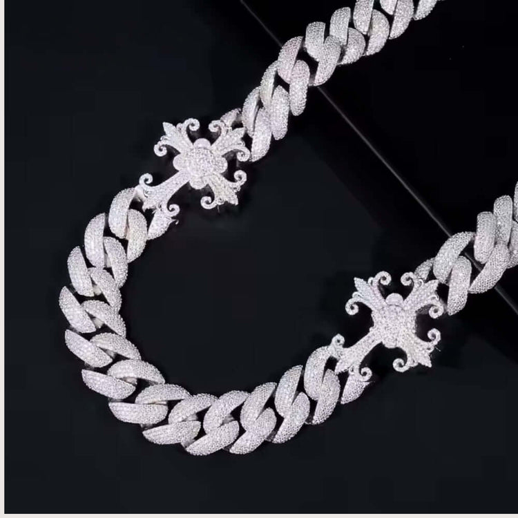 The Moissanite Cross Cuban Link Chain - 18mm is a thick, 925 sterling silver necklace with sparkling VVS moissanite stones and two large ornate cross pendants, displayed on a black surface.