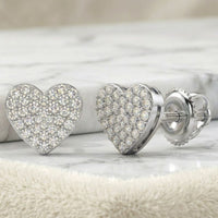 A close-up of 1/3CTW Natural Diamond Heart Earrings in sterling silver, adorned with sparkling diamonds, displayed on a soft beige fabric.