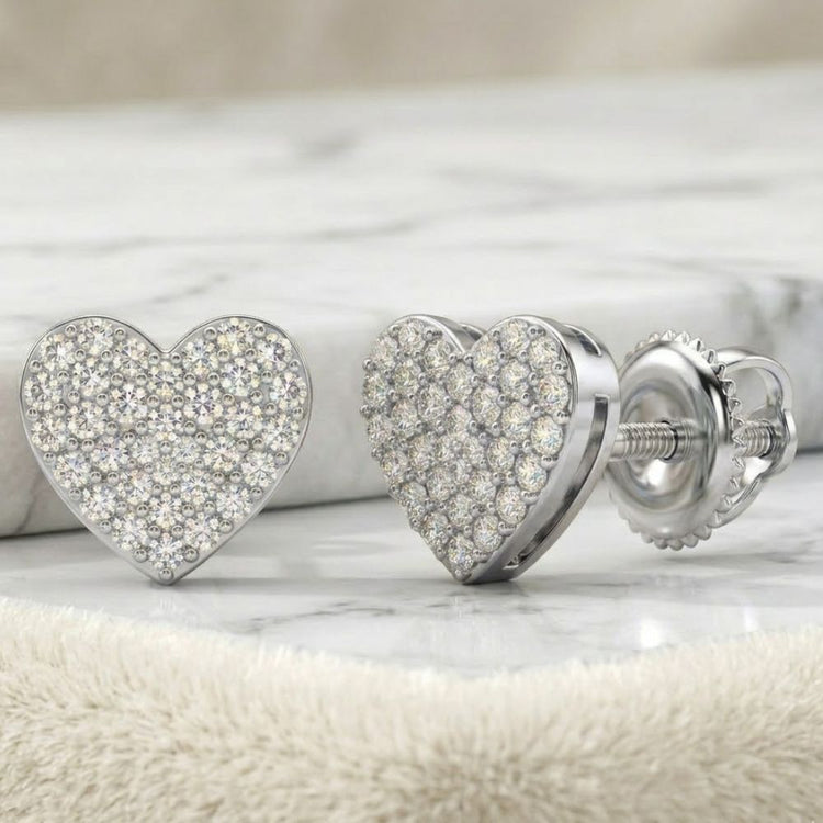 A close-up of 1/3CTW Natural Diamond Heart Earrings in sterling silver, adorned with sparkling diamonds, displayed on a soft beige fabric.
