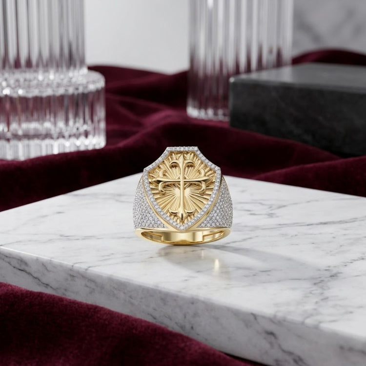 The 10k Gold 7/8 CTTW Diamond Cross Men’s Ring rests on a white marble surface, its natural diamonds sparkling in 10k yellow gold, surrounded by glass columns and deep red velvet fabric in the background.