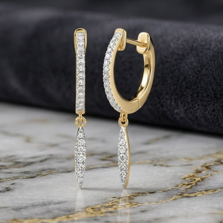 A pair of 10k White Gold Diamond Drop Dangle Earrings, featuring elongated, diamond-studded dangles suspended from classic hoops and displayed on a marble surface against a dark, textured fabric background—these dazzling earrings seamlessly combine elegance with modern sophistication.