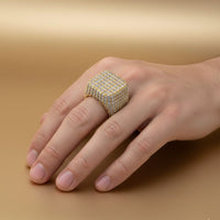 A hand showcases the Square Pavé Diamond Ring – 18 CT Gold Statement, featuring many sparkling diamonds, against a smooth light brown background.