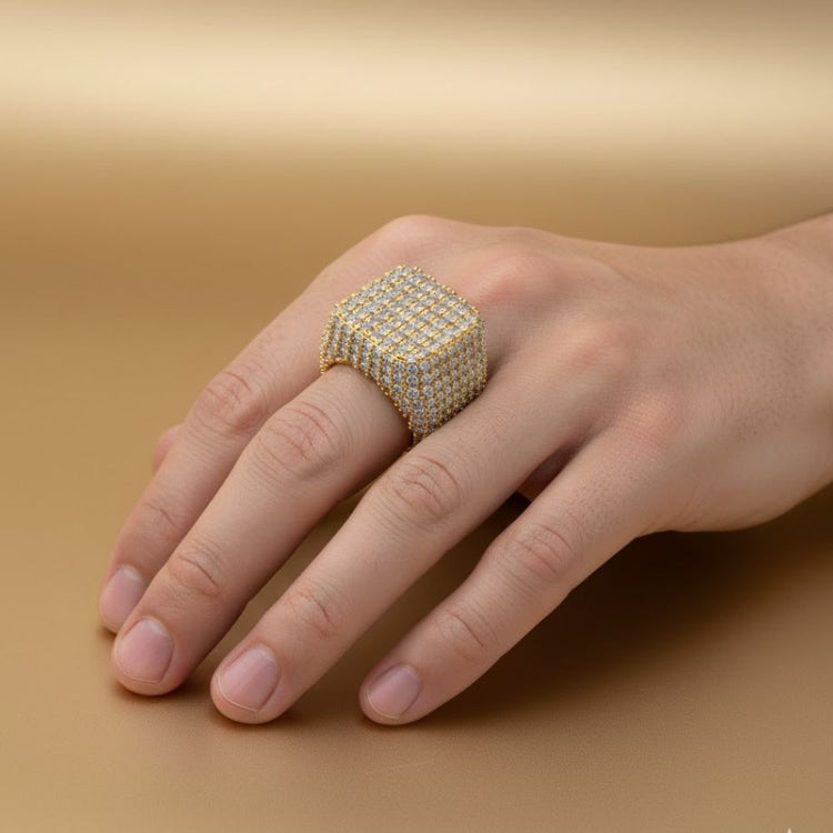 A hand showcases the Square Pavé Diamond Ring – 18 CT Gold Statement, featuring many sparkling diamonds, against a smooth light brown background.