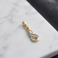 A beautiful 1/20 CTW Diamond Infinity Pendant in 10k gold, featuring an elegant twisted design with natural diamonds, rests on a white marble surface with part of a dark fabric visible in the background.