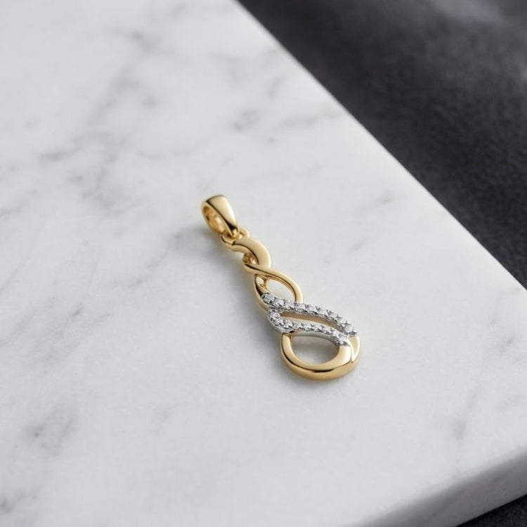 A beautiful 1/20 CTW Diamond Infinity Pendant in 10k gold, featuring an elegant twisted design with natural diamonds, rests on a white marble surface with part of a dark fabric visible in the background.