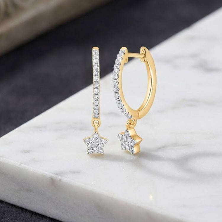 Introducing our 10K Gold Diamond Star Hoop Earrings 1/5 CTTW—delicate hoop earrings crafted from 10K yellow gold, each adorned with a shimmering, dangling star-shaped charm encrusted with clear diamonds. These elegant earrings are beautifully showcased against a striking white and black marble surface.