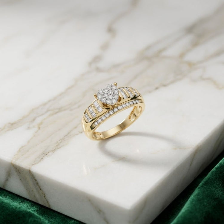 A 10k Gold Round Diamond Heart Engagement Ring rests elegantly on a marble surface, featuring a heart-shaped cluster of diamonds atop the band and smaller diamonds along the sides, with a green velvet fabric nearby.