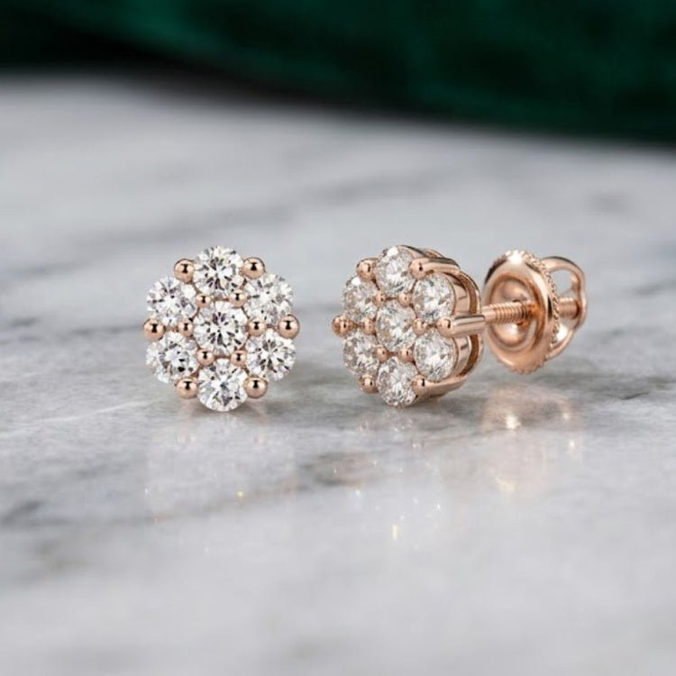 A pair of 10k Gold Diamond Flower Cluster Earrings (1 Cttw), each showcasing natural round diamonds in an elegant floral cluster design, displayed on a marble surface.