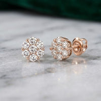 A pair of 10k Gold Diamond Flower Cluster Earrings (1 Cttw), each showcasing natural round diamonds in an elegant floral cluster design, displayed on a marble surface.
