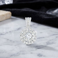 The 3/4 CTW Diamond Round Pendant in 14K gold showcases a dazzling central diamond encircled by sparkling accent diamonds. It is elegantly displayed on a marble surface, with a black cloth backdrop highlighting its brilliance.