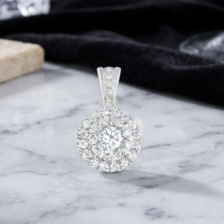 The 3/4 CTW Diamond Round Pendant in 14K gold showcases a dazzling central diamond encircled by sparkling accent diamonds. It is elegantly displayed on a marble surface, with a black cloth backdrop highlighting its brilliance.