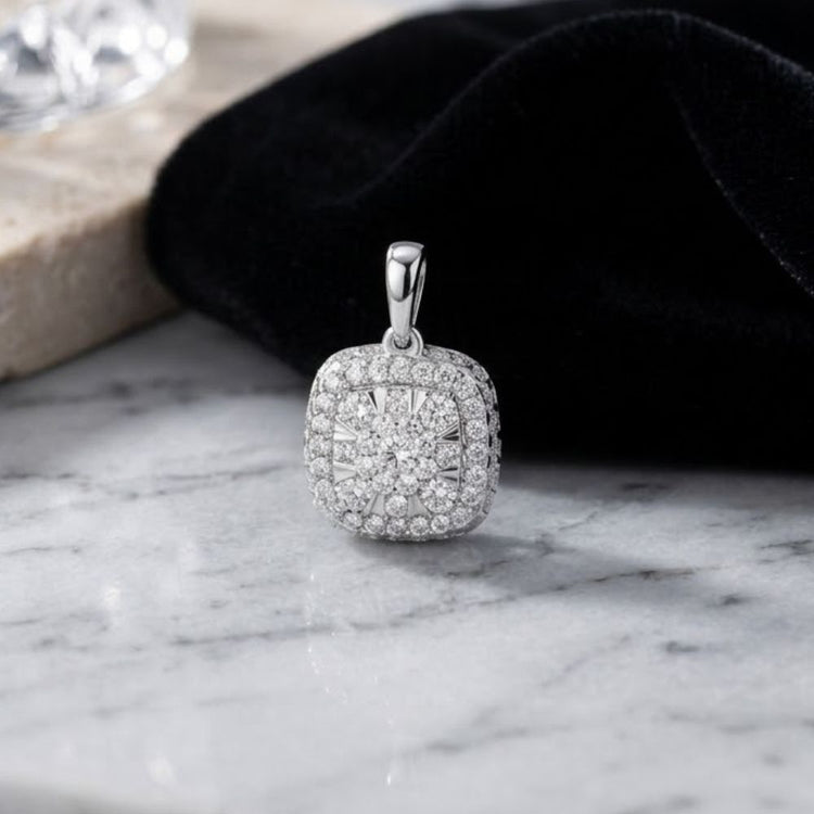 A 14K Gold 1/2 Ctw Diamond Cushion Pendant featuring a cushion-shaped halo of natural diamonds rests on a marble surface beside black velvet fabric.