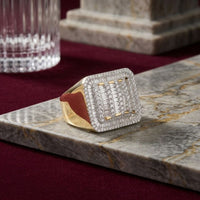 The 10k Yellow Gold Baguette Diamond Rectangle Ring, featuring a large rectangular face adorned with rows of sparkling diamonds, rests on a gray marble surface with a glass and stone object in the background. This eye-catching ring embodies elegance and modern style.
