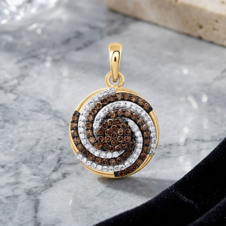 A 10k Yellow Gold Cognac Diamond Pendant (1/2 CTTW) with a spiral design featuring brown and white gemstones, including natural diamonds, is displayed on a marble surface beside a black cloth and a stone tile.